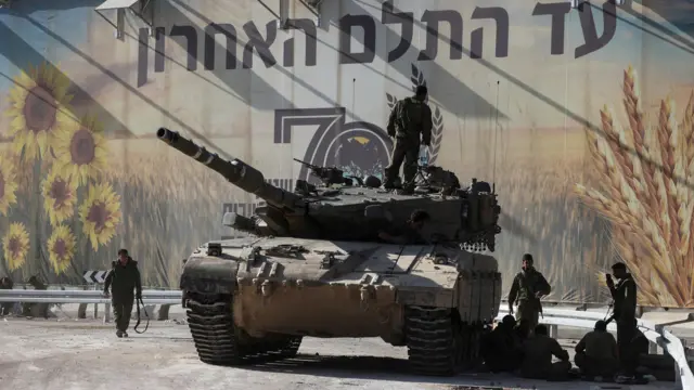 Солдаты около танка на фоне плаката