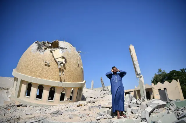 فلسطيني يرفع الأذان على أنقاض مسجد الأمين محمد، الذي قصفته غارة جوية إسرائيلية، في خان يونس
