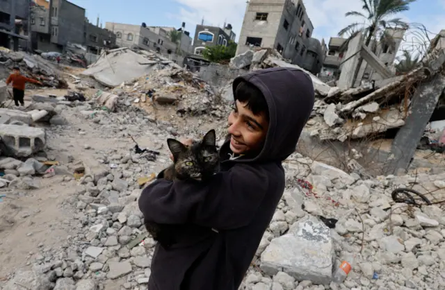 طفل فلسطيني يحمل قطة، بينما يقف على أنقاض المنازل التي دمرتها الضربات الإسرائيلية خلال الصراع، وسط الهدنة المؤقتة بين حماس وإسرائي
