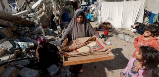 امرأة تحمل الخبز بجانب المنازل المدمرة في رفح جنوبي قطاع غزة.