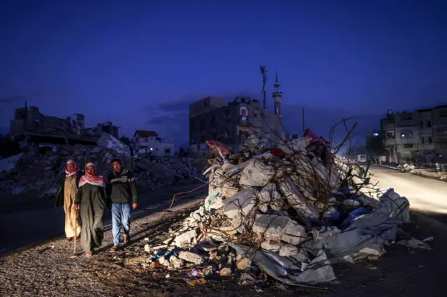 فلسطينيون يسيرون بجوار أنقاض المباني المدمرة في أعقاب القصف الإسرائيلي على رفح، في جنوب قطاع غزة فجر الجمعة 15 ديسمبر/كانون الأول 2023