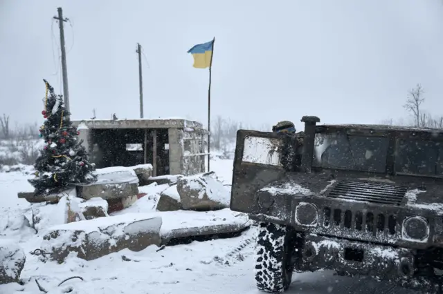 Украинские солдаты, проезжавшие мимо на броневике "Хамви", остановились, чтобы сфотографироваться у рождественской елки, установленной на разрушенном блокпосту.