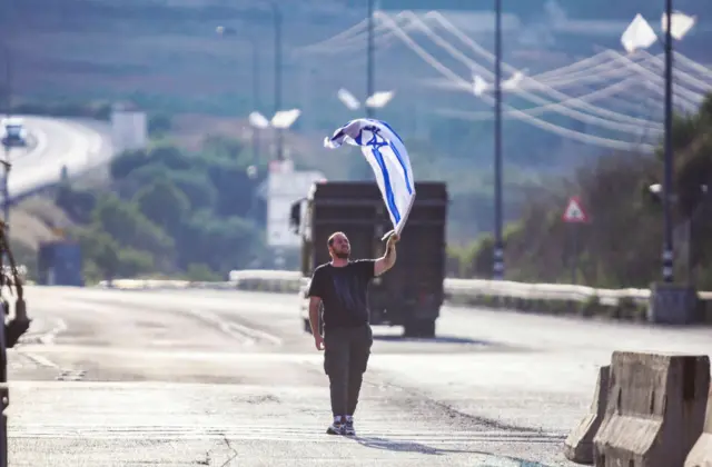 مستوطن إسرائيلي يلوح بالعلم الإسرائيلي أمام الفلسطينيين