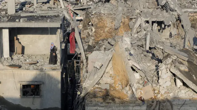 امرأة فلسطينية تقف في غرفة مدمرة في مبنى وهي تتفقد موقع الغارات الإسرائيلية، في خان يونس جنوبي قطاع غزة- 6 ديسمبر، 2023.