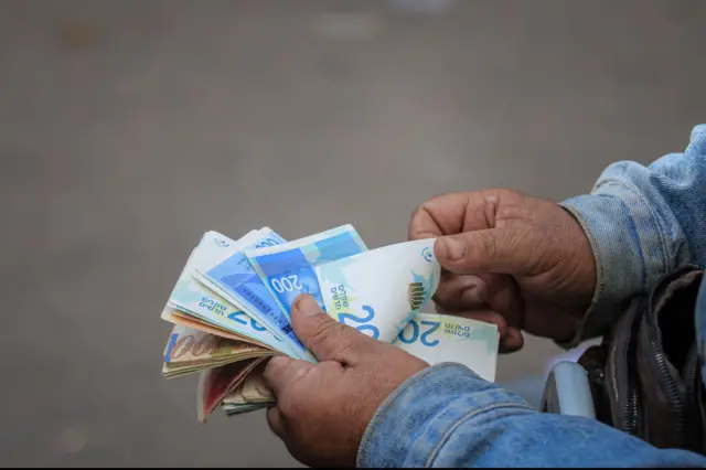 رجل يعد أوراقا نقدية إسرائيلية