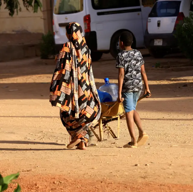 سودانيون يمشون بحثاً عن الماء أثناء الاشتباكات بين قوات الدعم السريع والجيش في شمال الخرطوم