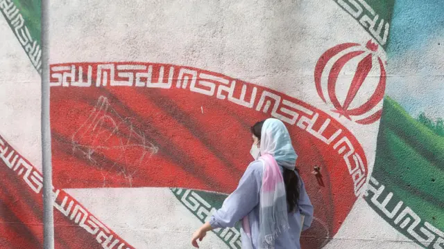 امرأة إيرانية تمشي أمام علم الجمهورية الإسلامية