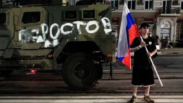 Человек с российским флагом на фоне БТР в Ростове-на-Дону