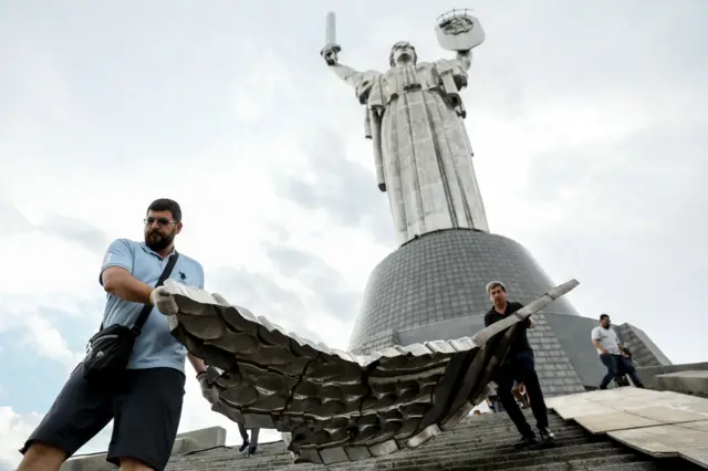 Двое рабочих несут часть герба