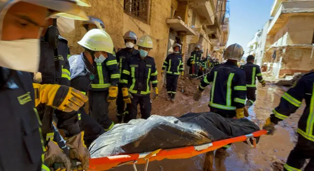 طاقم فريق إنقاذ مصري يحملون جثة أثناء سيرهم في الوحل بين المباني المدمرة في درنة