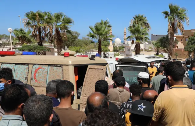 سيارة إسعاف تابعة للهلال الأحمر وحولها سكان ينتظرون نقل رفات ضحايا الفيضانات، الذين جرفتهم المياه إلى الشاطئ