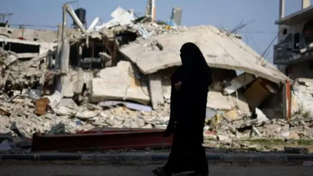 سيدة تسير بجانب أنقاض منزل دمرته غارة إسرائيلية في رفح، بالقرب من الحدود بين غزة ومصر
