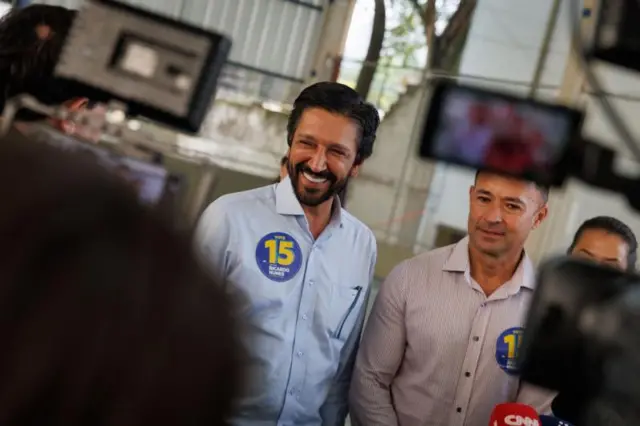 Ricardo Nunes e Mello Araújo sorrindo e rodeados por câmeras e jornalistas