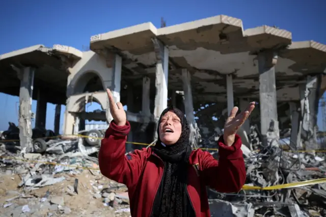 امرأة فلسطينية متأثرة، تقف أمام مبنى مدمر في مخيم المغازي للاجئين وسط قطاع غزة في 16 يناير/كانون الثاني 2024،