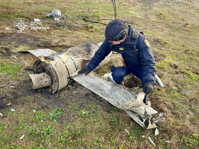 Мужчина в синей форме с украинскими знаками различия осматривает обломок