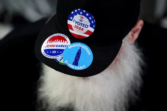 Eleitor com barca branca comprida veste boné com adesivos indicando que votou na eleição dos EUA