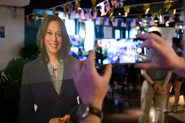 Pessoa tira foto de cartaz de Kamala Harris