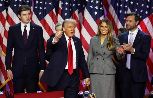 Donald Trump gesticula ao lado de sua esposa, Melania Trump, seu filho, Barron Trump, e o candidato republicano a vice-presidente, JD Vance, após os primeiros resultados da eleição presidencial de 2024 dos EUA, no Palm Beach County Convention Center, em West Palm Beach, Flórida, EUA, em 6 de novembro de 2024.