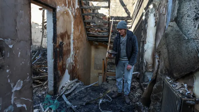 Человек в шапке осматривает выгоревший и искореженный
