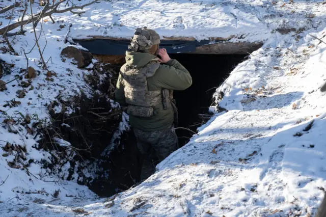 Украинский военнослужащий стоит в окопе посреди заснеженного поля