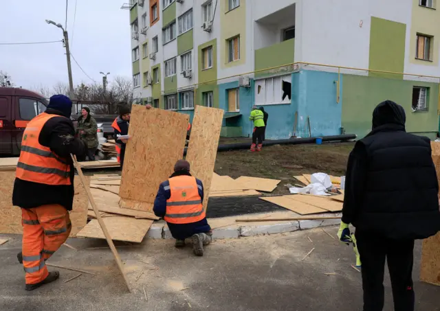 Сотрудники харьковских коммунальных служб готовятся закрывать окна в жилом доме, пострадавшем во время российского обстрела в среду