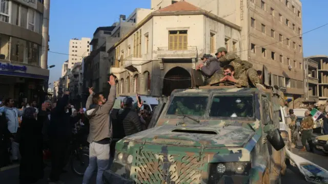 सीरिया में जश्न मनाते कई लोग और विद्रोही