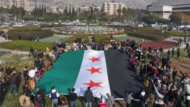 Watu wameshikilia bendera kubwa ya upinzani wa Syria kwenye uwanja wa Umayyad mjini Damascus
