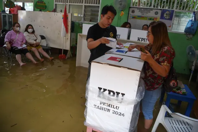 Warga memasukan surat suara Pemilu 2024 ke kotak suara saat banjir yang menggenang di TPS 028 Jelambar, Jakarta Barat, Rabu (14/2/2024).