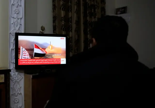 شخص يشاهد الأخبار على شاشة تلفزيون يديرها الحوثيون بعد تعرض سفينة مسجلة في المملكة المتحدة لهجوم في البحر الأحمر