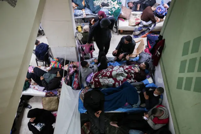 فلسطينيون أصيبوا في غارات إسرائيلية يستلقون على الأسرة بينما يحتمي النازحون في مستشفى شهداء الأقصى