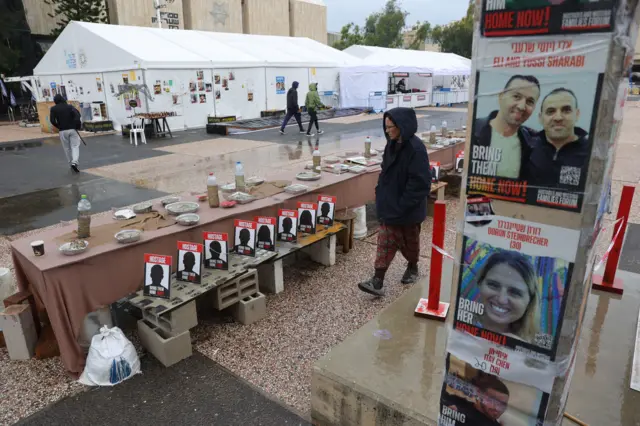 أشخاص يقفون بالقرب من طاولة محاطة بكراسي فارغة ترمز إلى الرهائن الذين تحتجزهم حماس في غزة