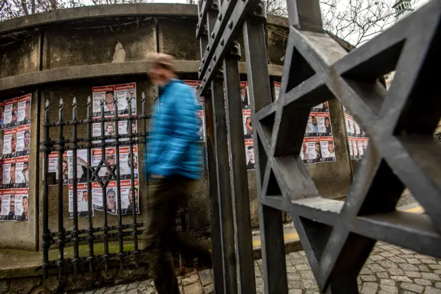 أشخاص يسيرون بجوار ملصقات تظهر أشخاصاً مخطوفين في غزة