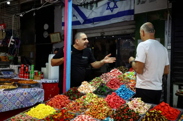 أشخاص بالقرب من بقالة ترفع العلم الإسرائيلي بعد أن أطلقت إيران طائرات مسيرة وصواريخ باتجاه إسرائيل في تل أبيب.