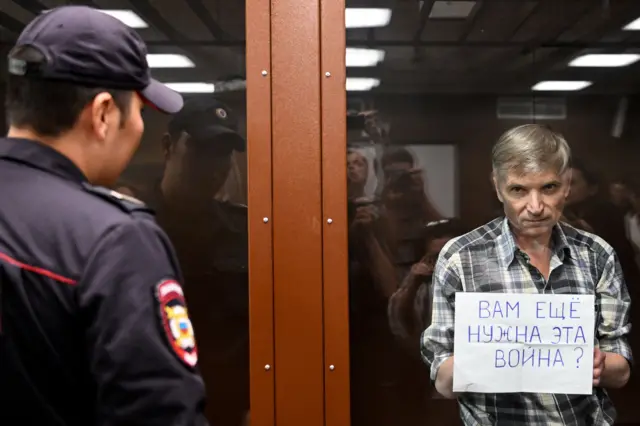 Алексей Горинов в стеклянной клетке в зале суда в 2002 году с плакатом "Вам еще нужна эта война?"