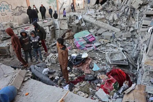 أشخاص يقفون بجوار أنقاض مدرسة تؤوي فلسطينيين نازحين، دمرتها غارة إسرائيلية على مدينة غزة (في 13 يناير/كانون الثاني 2025)