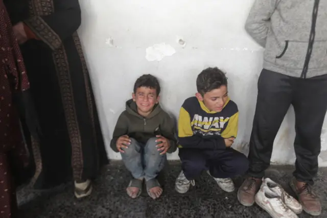 أطفال فلسطينيون يبكون خلال نقل جثث أقاربهم الذين قُتلوا في الهجوم الإسرائيلي على مدرسة "الفلاح" في حي الزيتون إلى مستشفى المعمدان الأهلي في مدينة غزة في 16 يناير/كانون الثاني 2025.