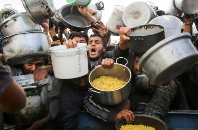 فلسطينيون يتجمعون لتلقي الطعام الذي يجهزه أحد المطابخ الخيرية، قبل سريان وقف إطلاق النار بين حماس وإسرائيل، في خان يونس، جنوب قطاع غزة، 17 يناير/كانون الثاني 2025.