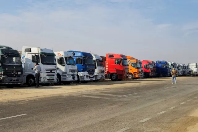 سائق يسير بجوار شاحنات تحمل مساعدات مصطفة بالقرب من معبر رفح في انتظار العبور إلى قطاع غزة