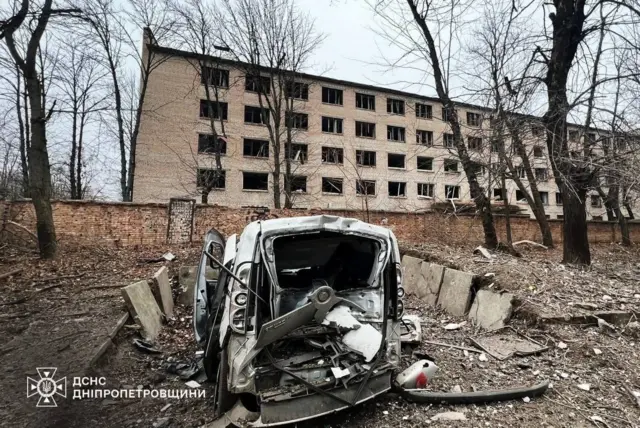 Поврежденный автомобиль на фоне дома с выбитыми окнами.