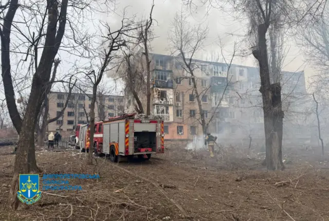 Пятиэтажное здание, пострадавшее от ракетного удара, перед зданием стоят пожарные машины.