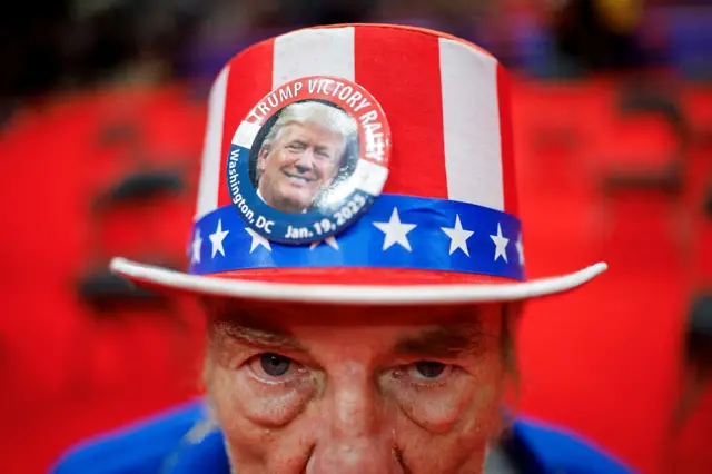 Um homem usa um chapéu com a bandeira dos EUA e uma foto de Trump