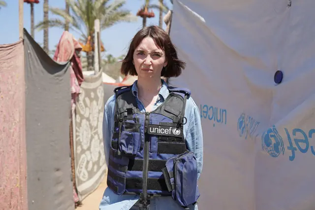 تس اینگرام، سخنگوی یونیسف مقابل چادرهای پناهجویان ایستاده است.