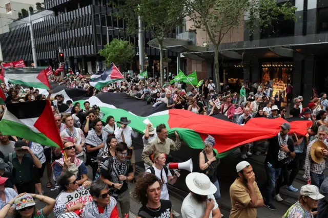 متظاهرون يحملون علمًا فلسطينياً كبيراً خلال مسيرة في سيدني في أستراليا