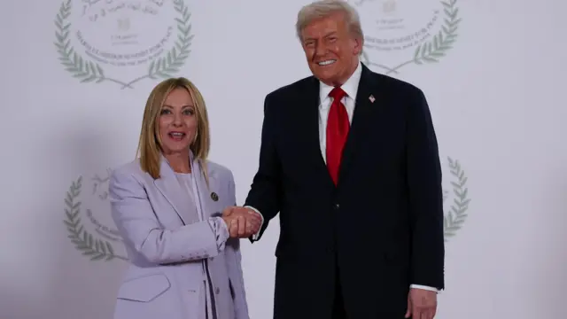 Джорджа Мелони в лиловом костюме и Дональд Трамп держатся за руки и улыбаются