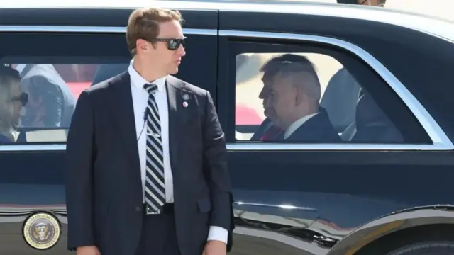 Дональд Трамп в машине, перед дверцей стоит охранник