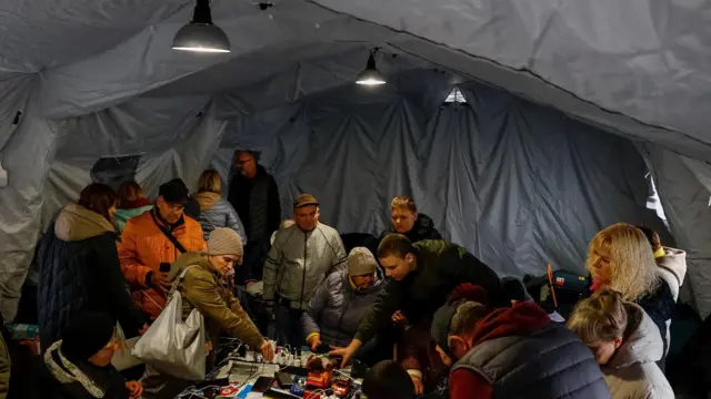 Большая группа людей в палатке склонилась над столом с удлинителем
