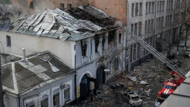 Снимок здания детского сада с высоты, видна большая пробоина в крыше, к ней тянется лестница от пожарной машины