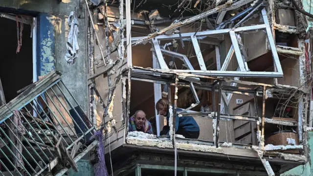 Женщина и более старший мужчина выглядывают с балкона без стекол на верхнем этаже