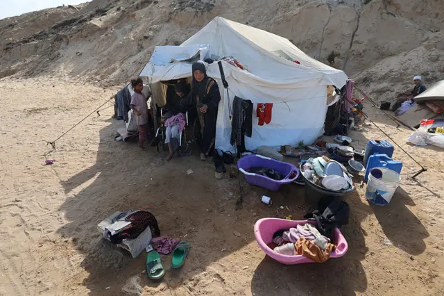 صورة بتاريخ 4 أكتوبر/تشرين الأول 2025، لنازحين فلسطينيين يحتمون بجوار خيمة نصبوها قرب طريق ساحلي شمال غرب مخيم النصيرات للاجئين، بعد نزوحهم جنوباً بعيد إعلان إسرائيل إغلاق طريق الرشيد المؤدي إلى شمال قطاع غزة.