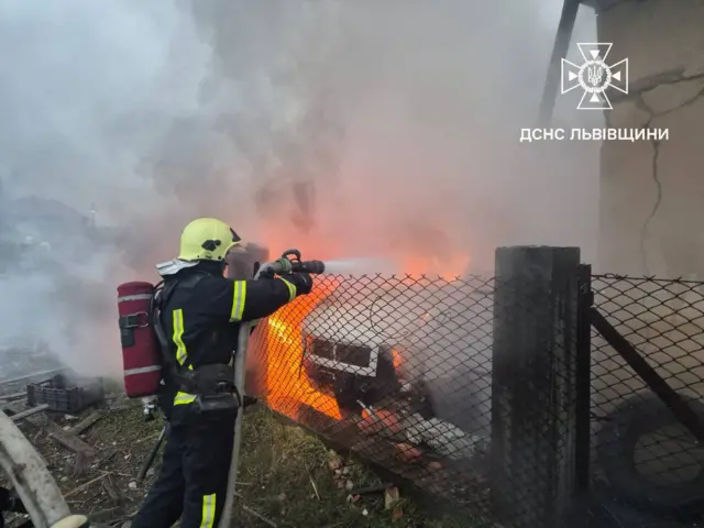 Пожарный тушит горящий автомобиль